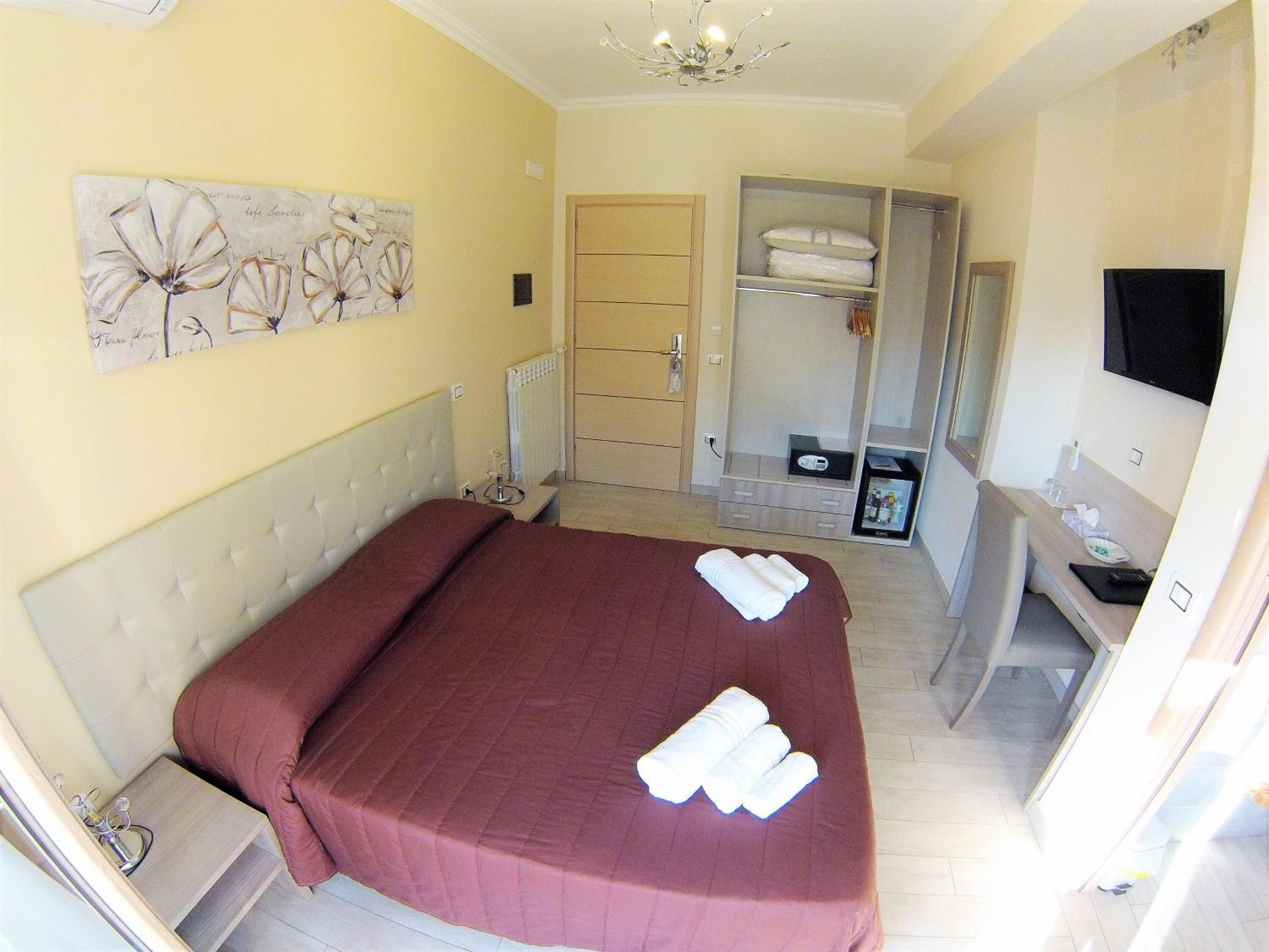 Habitación de hotel con una cama grande, un armario, un escritorio con silla, un televisor y un espejo.