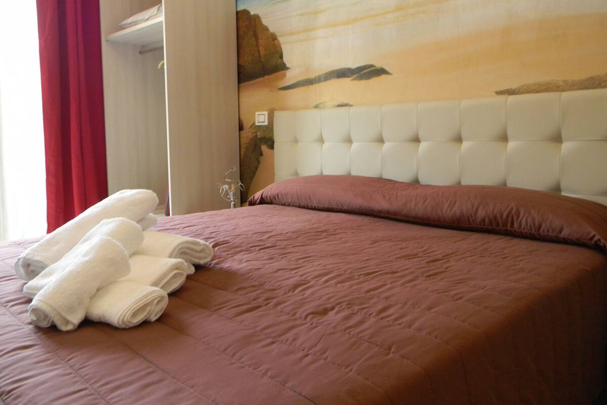 A hotel room with a bed, a headboard, and a painting of a beach scene.
