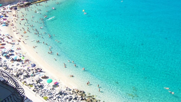 A beach with clear turquoise water, rocky shoreline, and umbrellas. - Tropeacentro (Tropea)