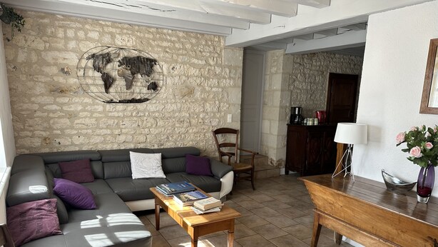 A living room with a stone wall, a sofa, a coffee table, and a wooden side table. - Chambres d'hôtes Le Puy d'Anché (Sauzé-Vaussais)