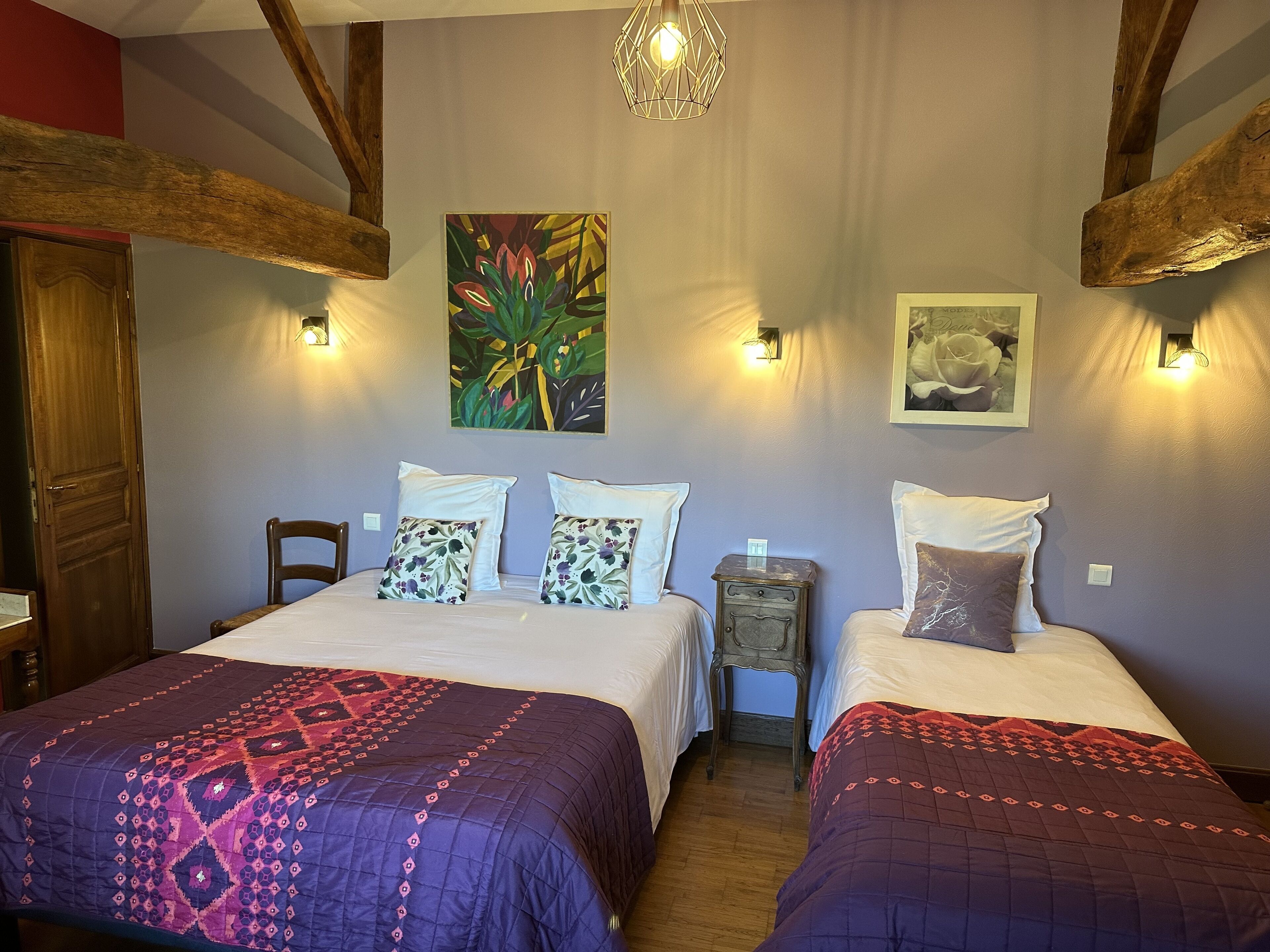Una habitación con dos camas, cada una con ropa de cama estampada, un cabecero de madera y una mesita de noche entre ellas. Hay luces fijadas a la pared y un cuadro grande sobre las camas.