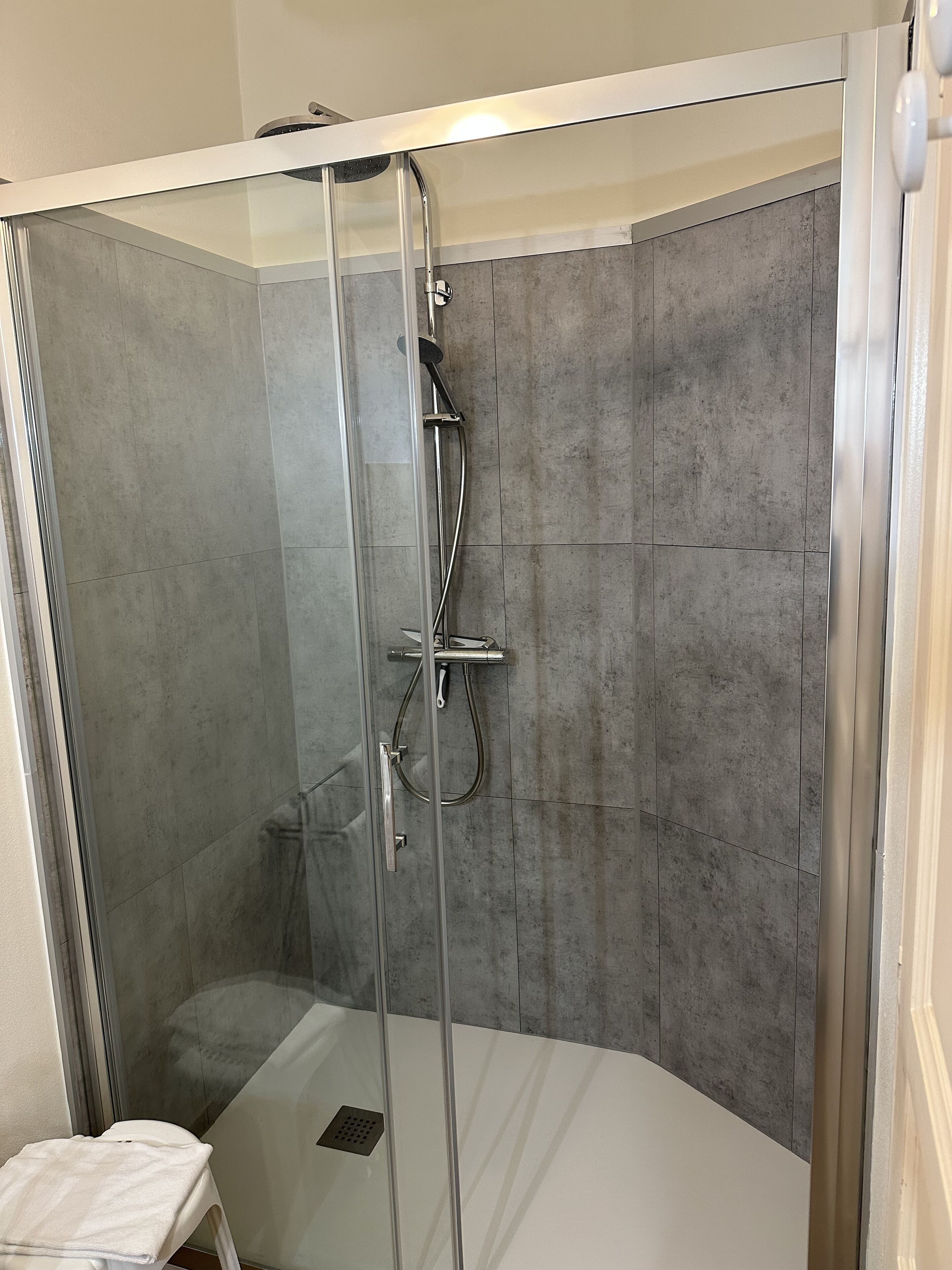 A glass-enclosed shower with a handheld showerhead and a handheld faucet.