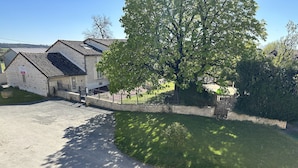 A stone building with a metal roof, a paved driveway, and a grassy area with a tree. - Chambres d'hôtes Le Puy d'Anché (Sauzé-Vaussais)