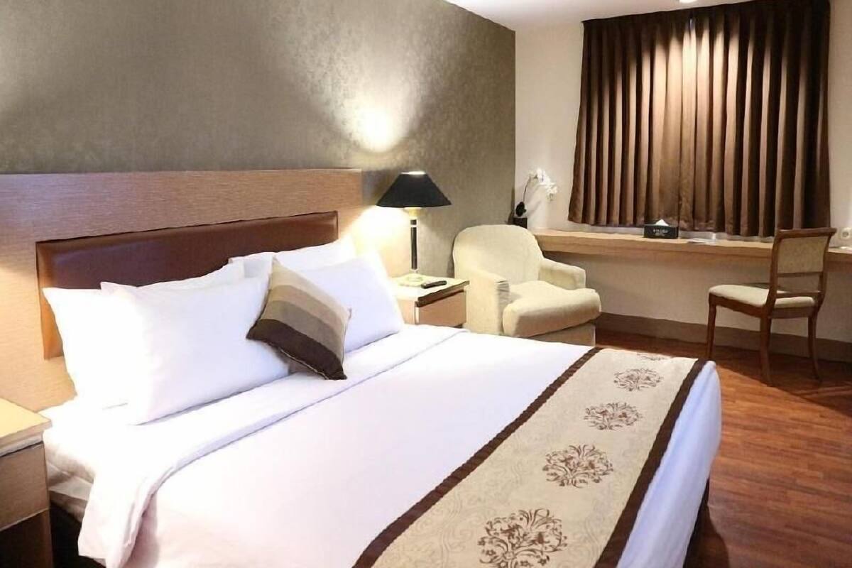 Una habitación de hotel con cama, escritorio, silla y ventana con cortinas.