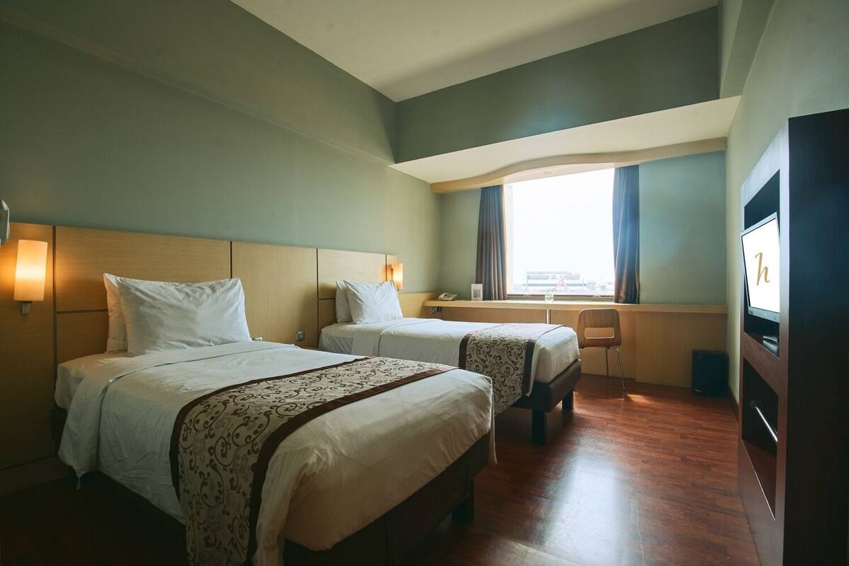 A hotel room with two beds, a desk, a chair, a TV, and a window with curtains.
