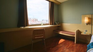 Ein Hotelzimmer mit großem Fenster, einem Holztisch, einer Bank und einem Bett.