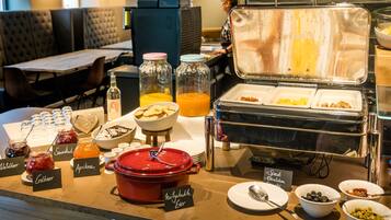 Un bufé con diversos alimentos y condimentos, incluidas conservas en frascos y una olla roja de comida.
