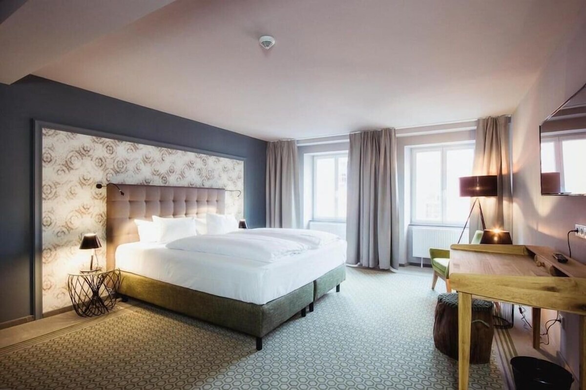 Une chambre d’hôtel avec un grand lit, un bureau, une chaise, une lampe et une fenêtre avec des rideaux.