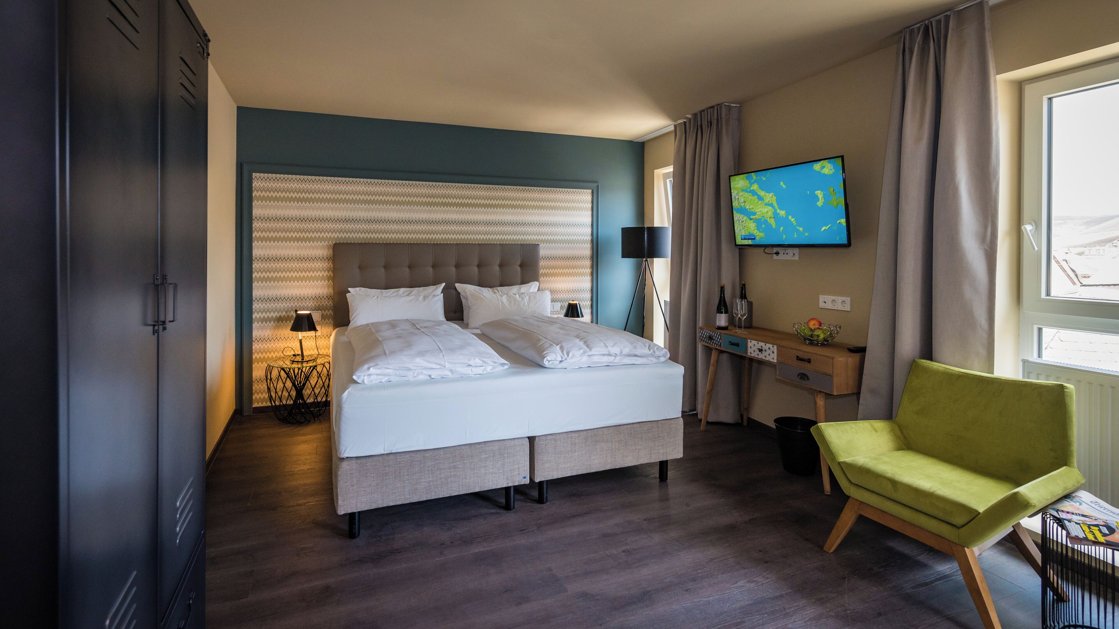 A hotel room with a bed, a desk, a chair, a TV, and a window.