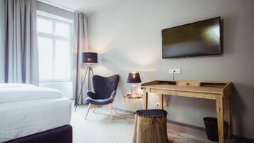 Habitación de hotel con cama, escritorio, silla, lámpara, televisor y ventana con cortinas.