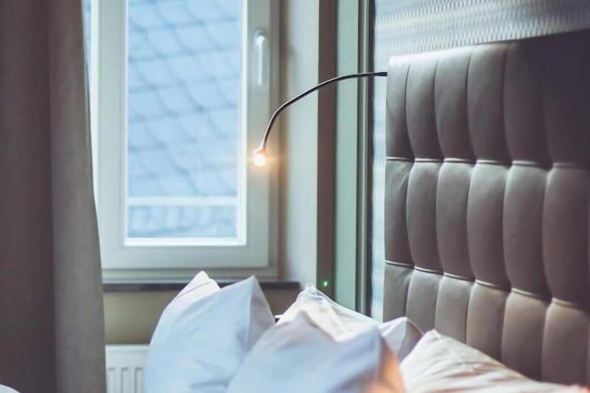 Une chambre à coucher avec une tête de lit capitonnée, une fenêtre avec des stores et une lampe de chevet.
