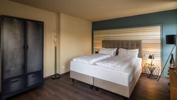 Habitación de hotel con cama, armario, lámpara de pie y mesita de noche con botella y vaso.