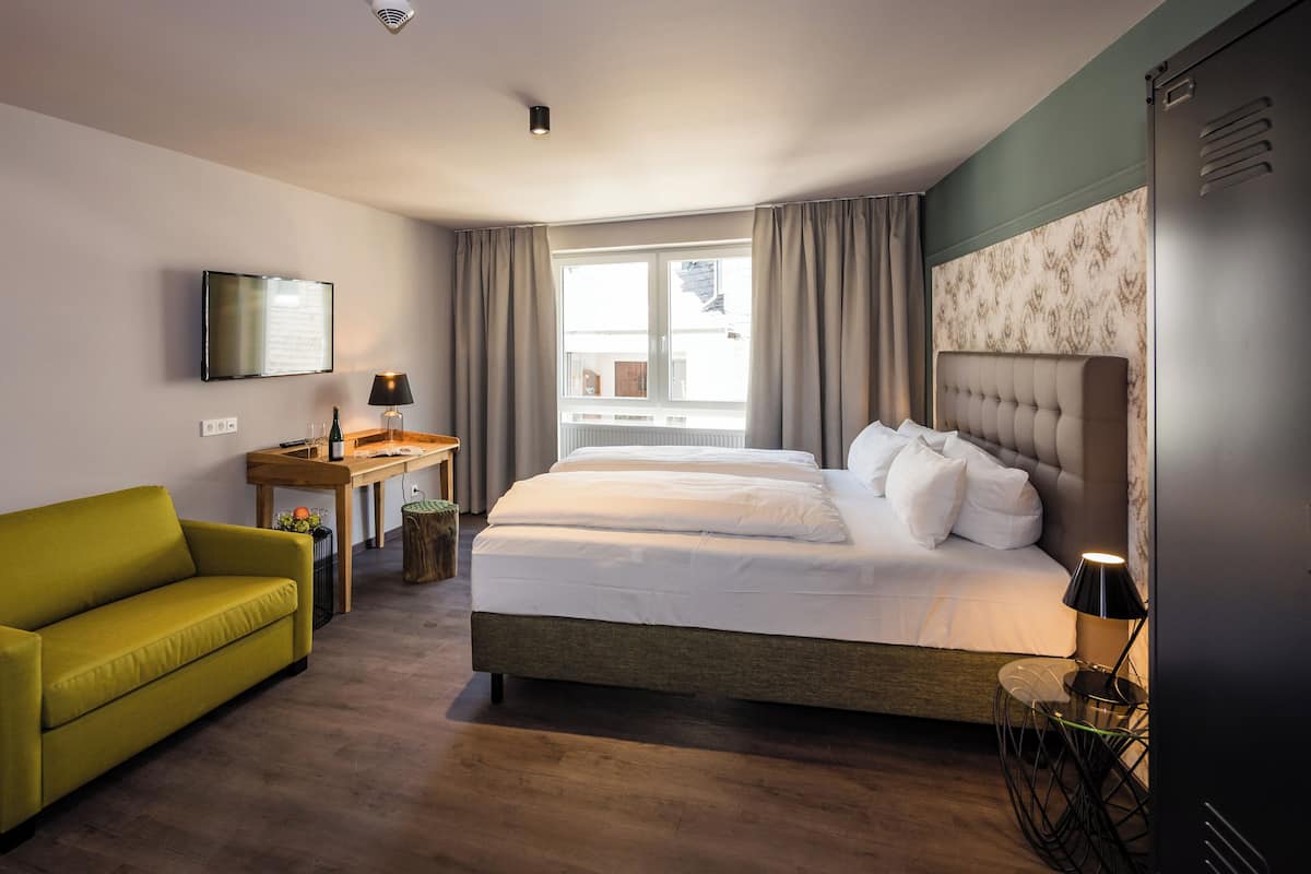 Une chambre d’hôtel avec un lit, un canapé, une télévision, un bureau et une fenêtre.