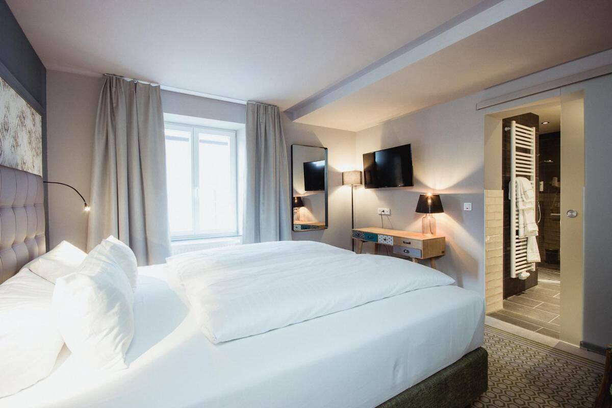 Une chambre d’hôtel avec un grand lit, un téléviseur à écran plat fixé au mur, un bureau avec une lampe et une salle de bain visible à travers une porte ouverte.