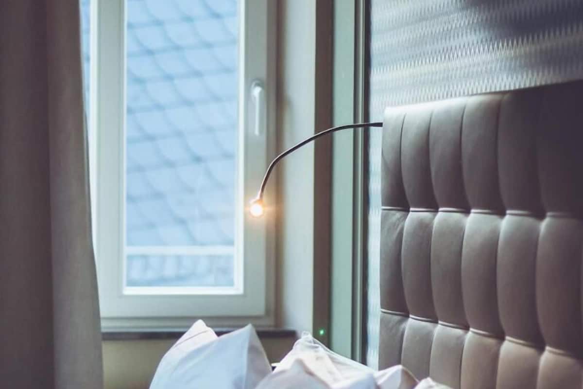 Une chambre à coucher avec une tête de lit capitonnée, une fenêtre avec des stores et une lampe de chevet.