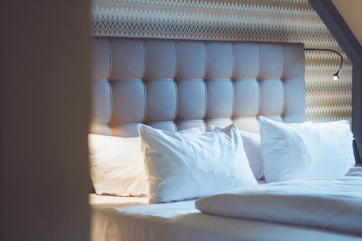 Una cama con cabecera capitonada, ropa de cama blanca y un papel tapiz estampado al fondo.