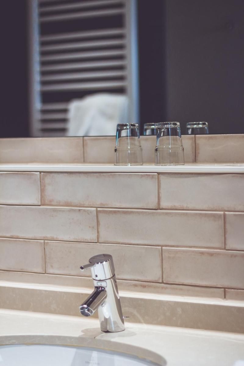 A bathroom sink with a chrome faucet and a shelf above it holding several clear glasses.