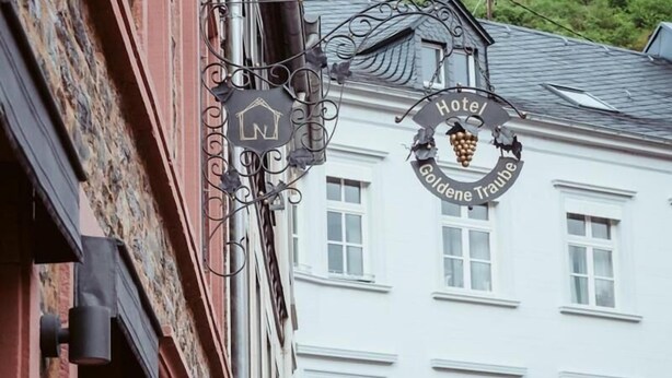 Een hotelschild met een logo en naam, een gebouw met een rode gevel, en een wit gebouw met ramen op de achtergrond.