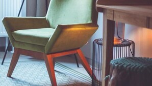 Een kamer met een groene fauteuil, een vloerlamp, een tafel en een klein rond tafeltje met een kaars.