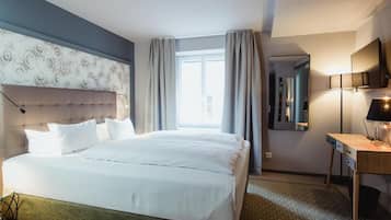A hotel room with a large bed, a desk with a lamp, a TV, and a window with curtains.