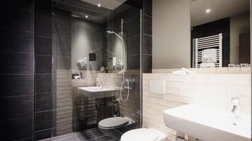 A modern bathroom with a glass-enclosed shower, a white sink, and a toilet.