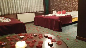Een hotelkamer met twee bedden, een tafel met kaarsen en rozenblaadjes, en een raam met gordijnen met een patroon.