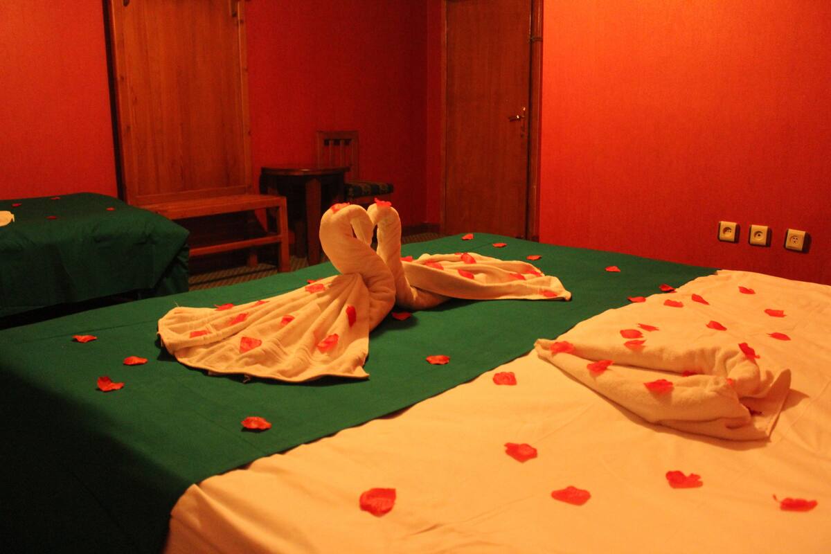 A hotel room with a bed adorned with rose petals and two towels shaped like swans.