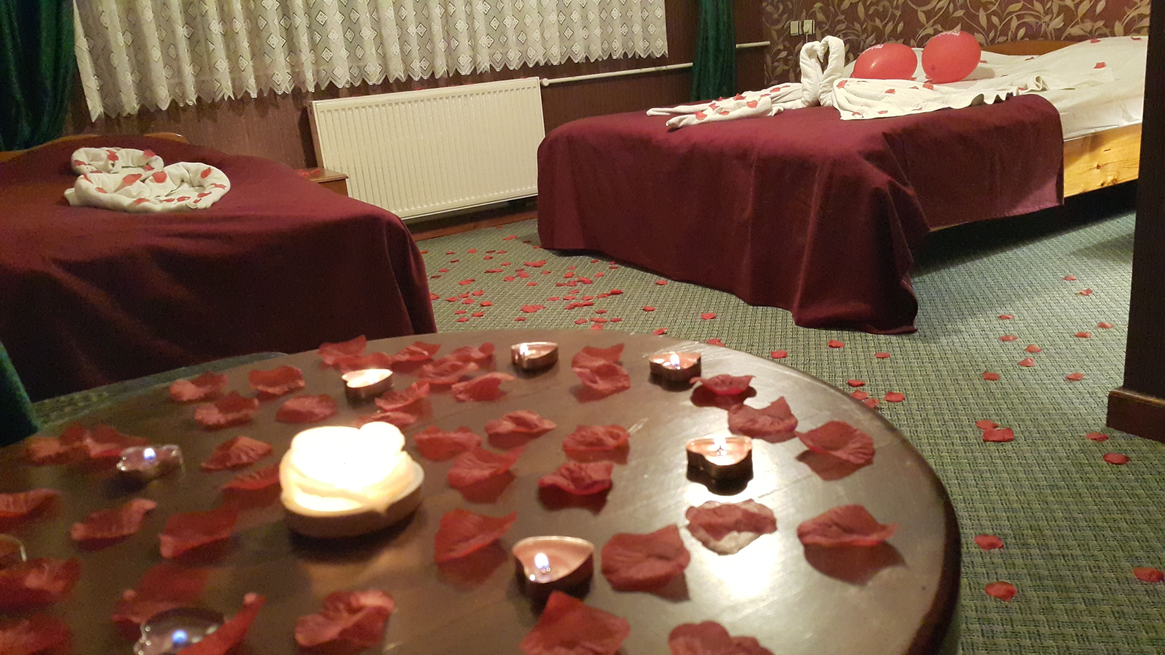 A hotel room with two beds, a round table with candles and rose petals, and a carpeted floor.