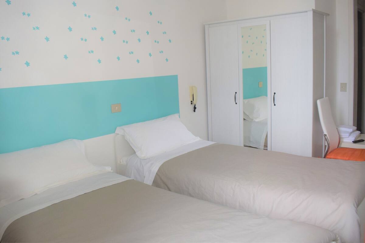A hotel room with two beds, a wardrobe, a mirror, and a wall with star decorations.