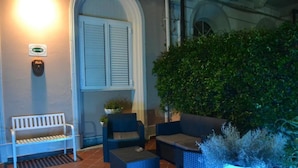 A seating area with a bench, two chairs, and a small table, surrounded by potted plants and a large bush. - Hotel Canarco (Viareggio)