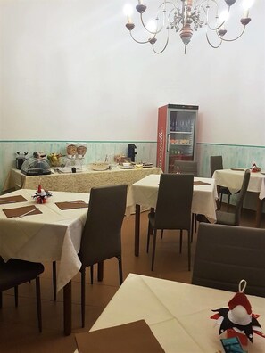 A restaurant with tables set for dining, a Coca-Cola refrigerator, and a chandelier. - Hotel Canarco (Viareggio)
