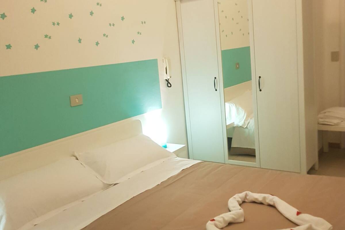 A neatly made bed with a brown bedspread and white pillows, a white wardrobe with a mirror, and star-shaped wall decals.