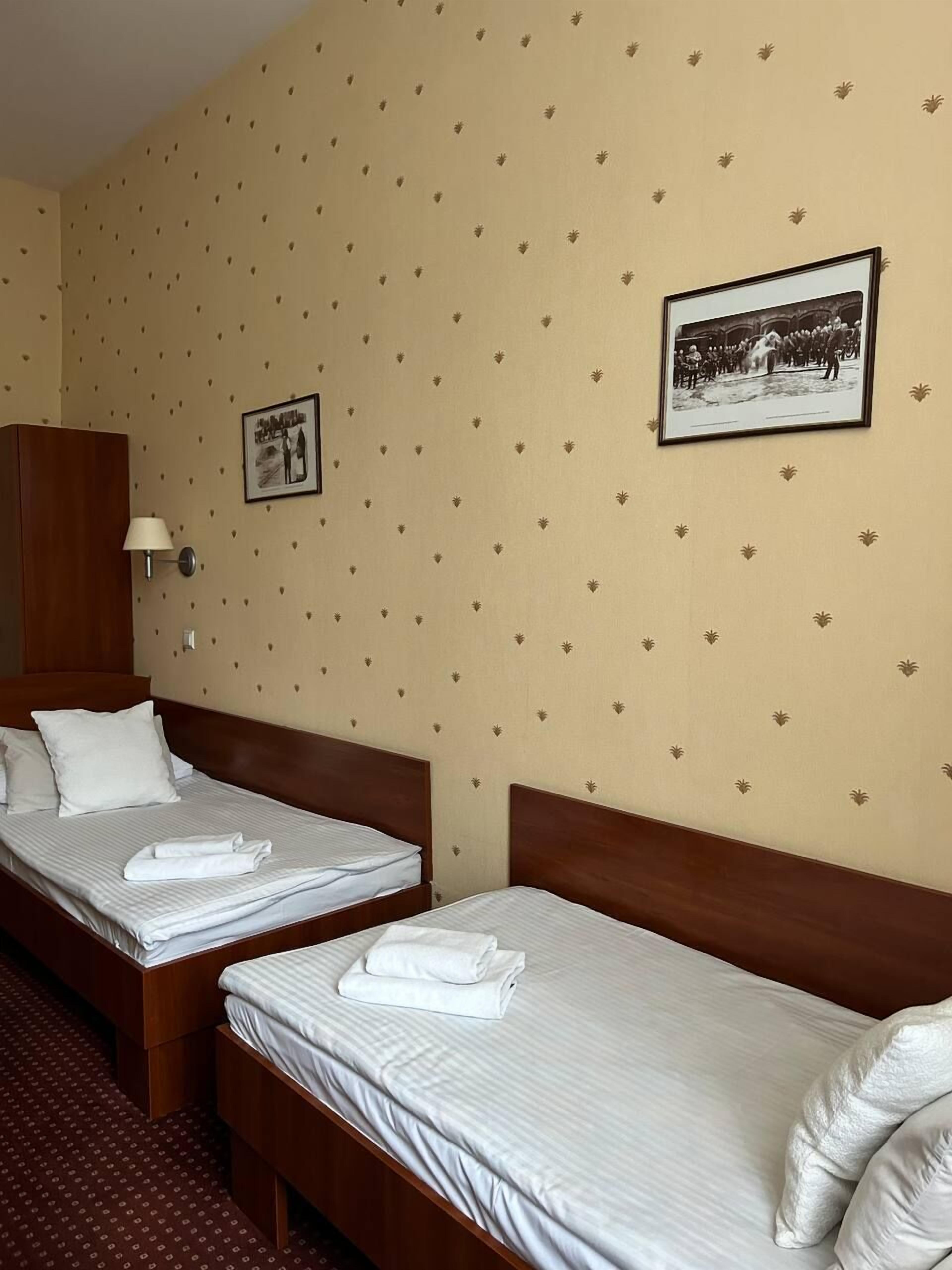 Una habitación de hotel con dos camas individuales, un armario de madera, una lámpara de pared y dos cuadros enmarcados.