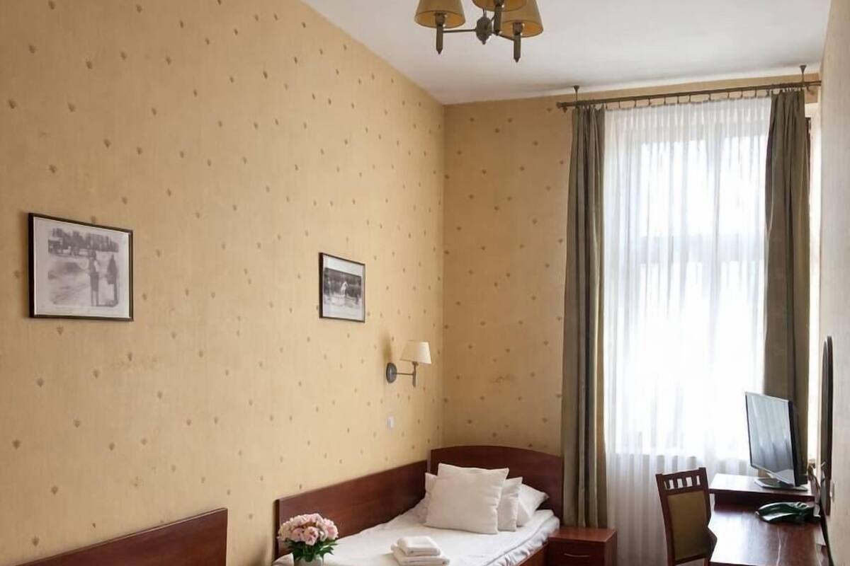 A hotel room with two single beds, a desk with a chair, a television, and a window with curtains.