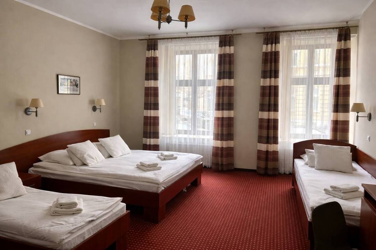 A hotel room with two beds, a desk, a chair, a lamp, a picture on the wall, and a window with curtains.