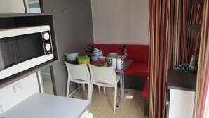 Una cocina compacta con microondas, una pequeña mesa de comedor con sillas y un banco rojo.