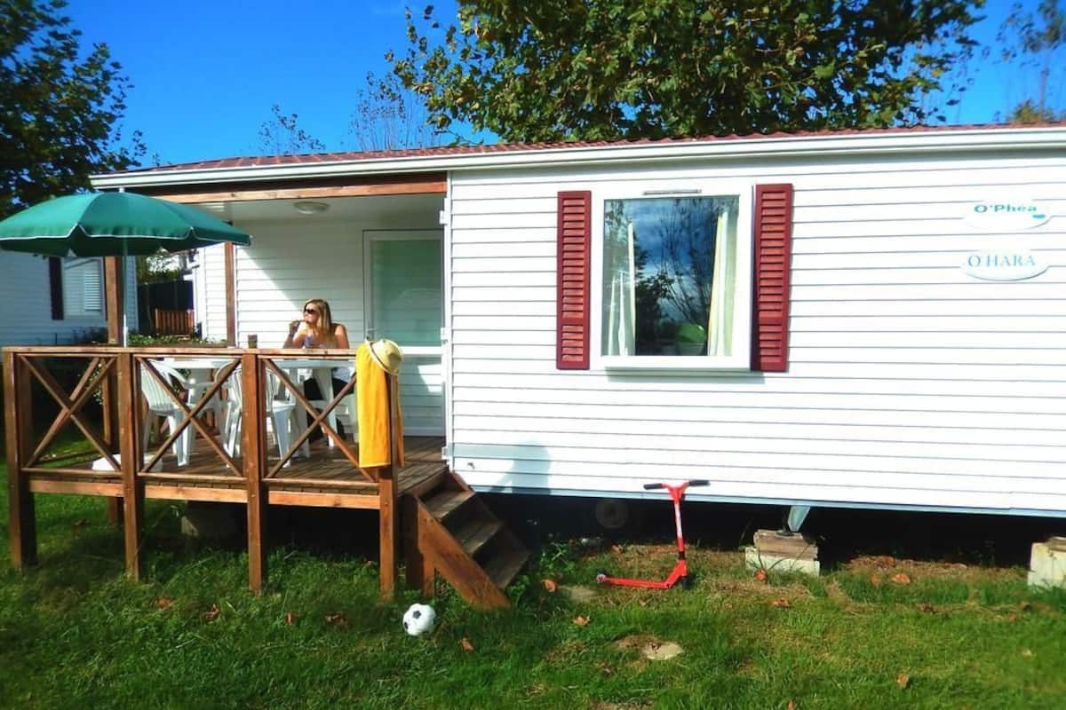 A mobile home with a porch, a green umbrella, and a red scooter.