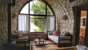 A cozy room with stone walls, a large arched window, a sofa, a small round table, and a bed. - Bkerzay (Deir Dourite)