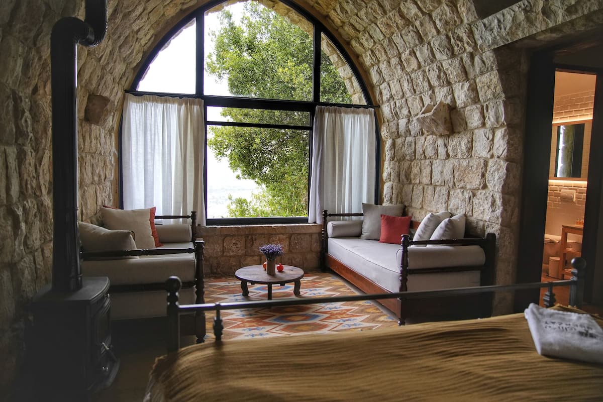 Ein gemütliches Zimmer mit Steinwänden, einem großen Bogenfenster, einer Couch, einem kleinen runden Tisch und einem Bett.