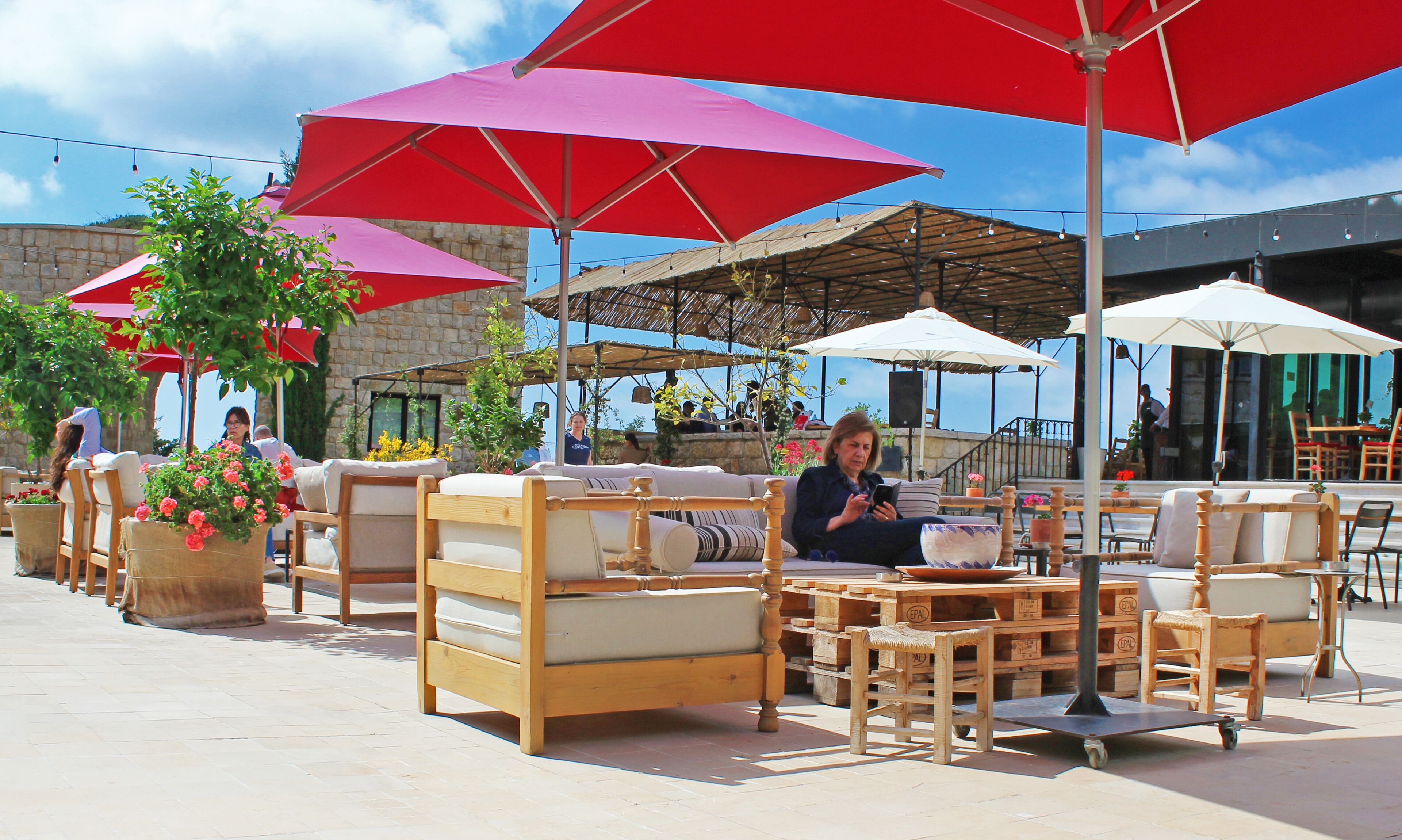 Outdoor seating with red umbrellas, wooden furniture, and potted plants.