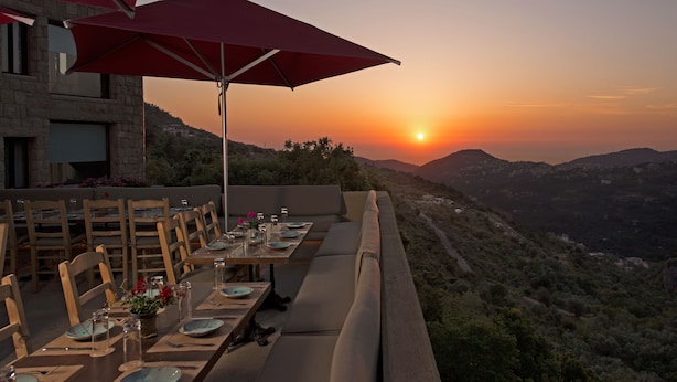 An outdoor dining area with tables set for a meal, overlooking a mountainous landscape during sunset. - Bkerzay (Deir Dourite)