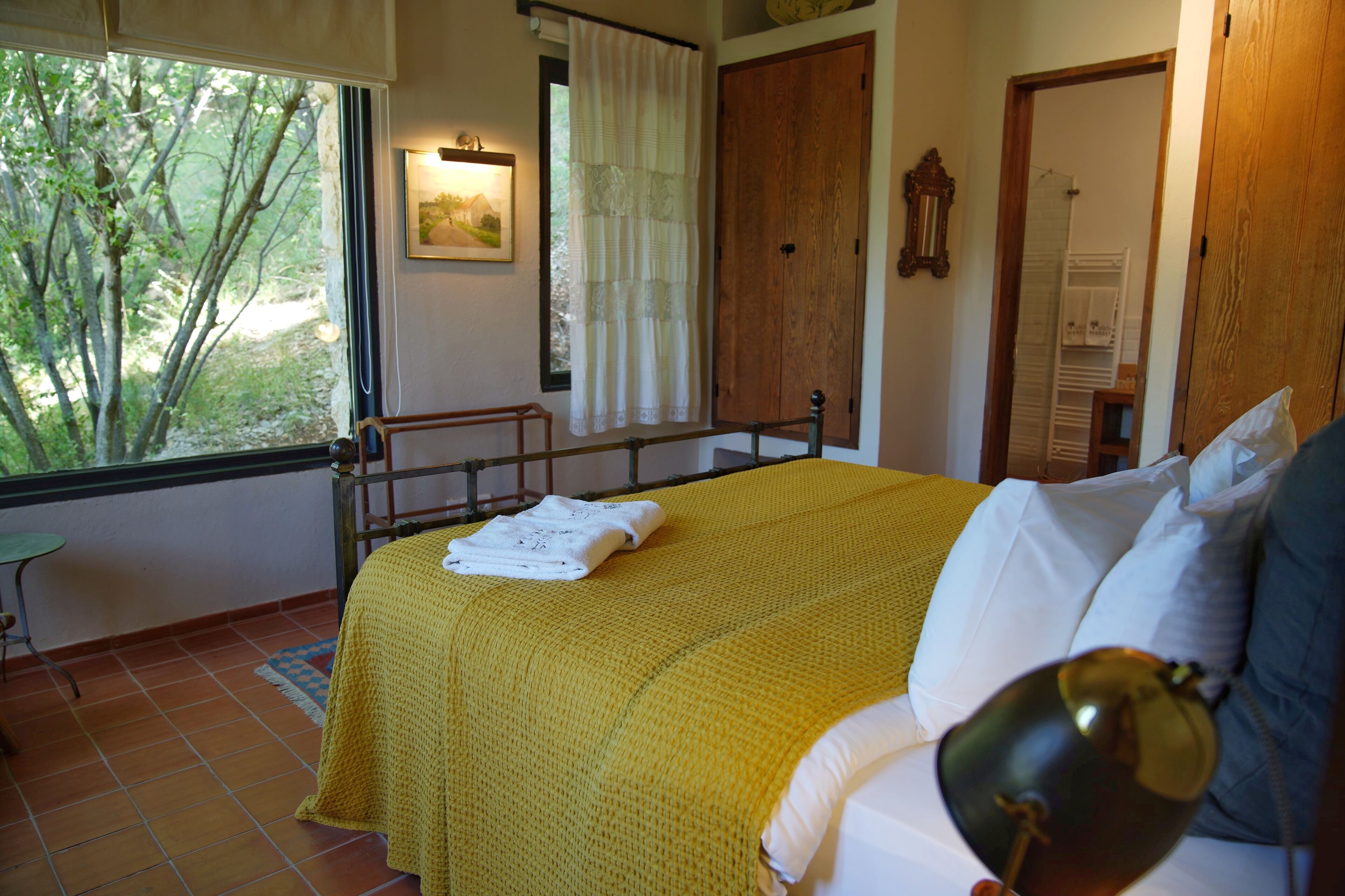 A bedroom with a bed, a bedside table, a window with a view of trees, and a door.