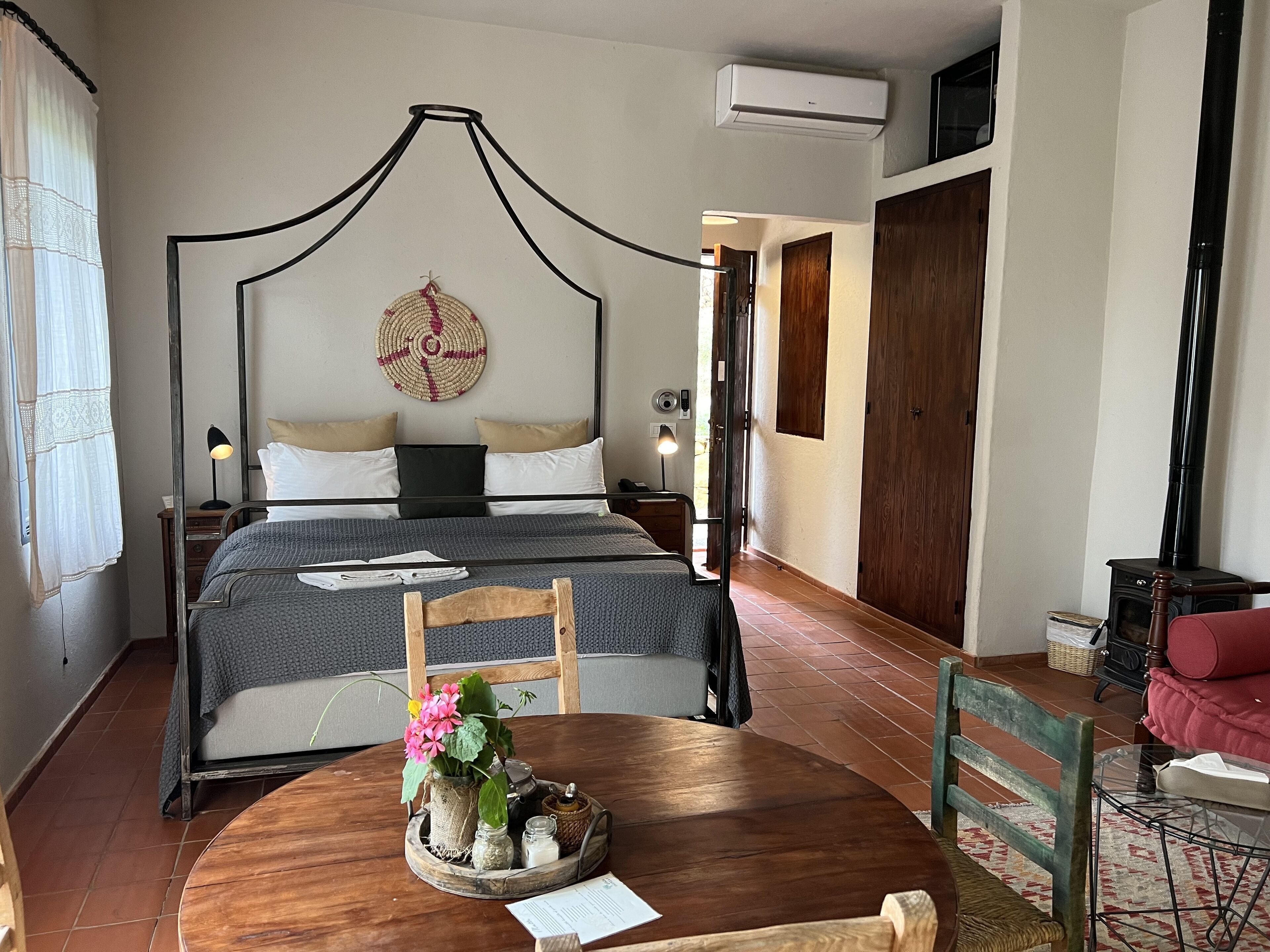 A bedroom with a four-poster bed, a wooden dining table with a vase of flowers, and a red sofa.