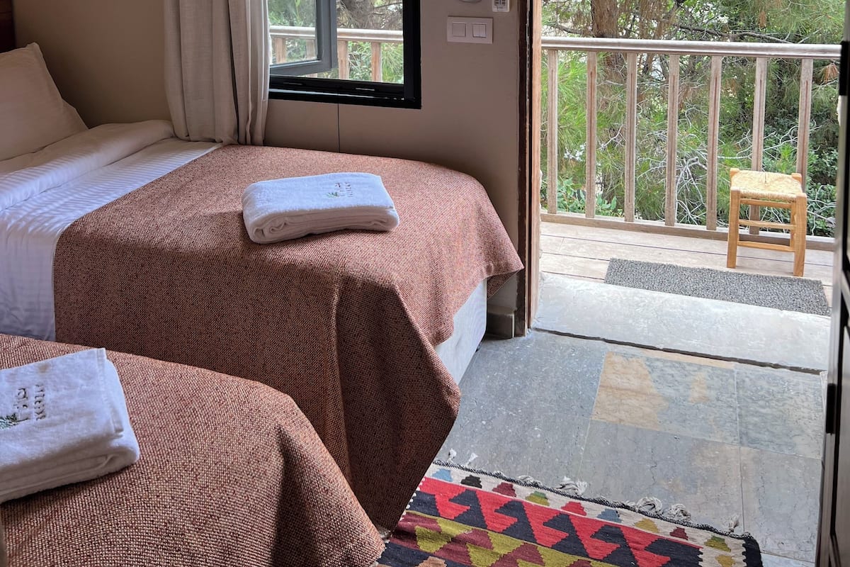 Ein Hotelzimmer mit Bett, einem Fenster mit Vorhängen, einem Feuerlöscher und einem Balkon mit einem Stuhl.