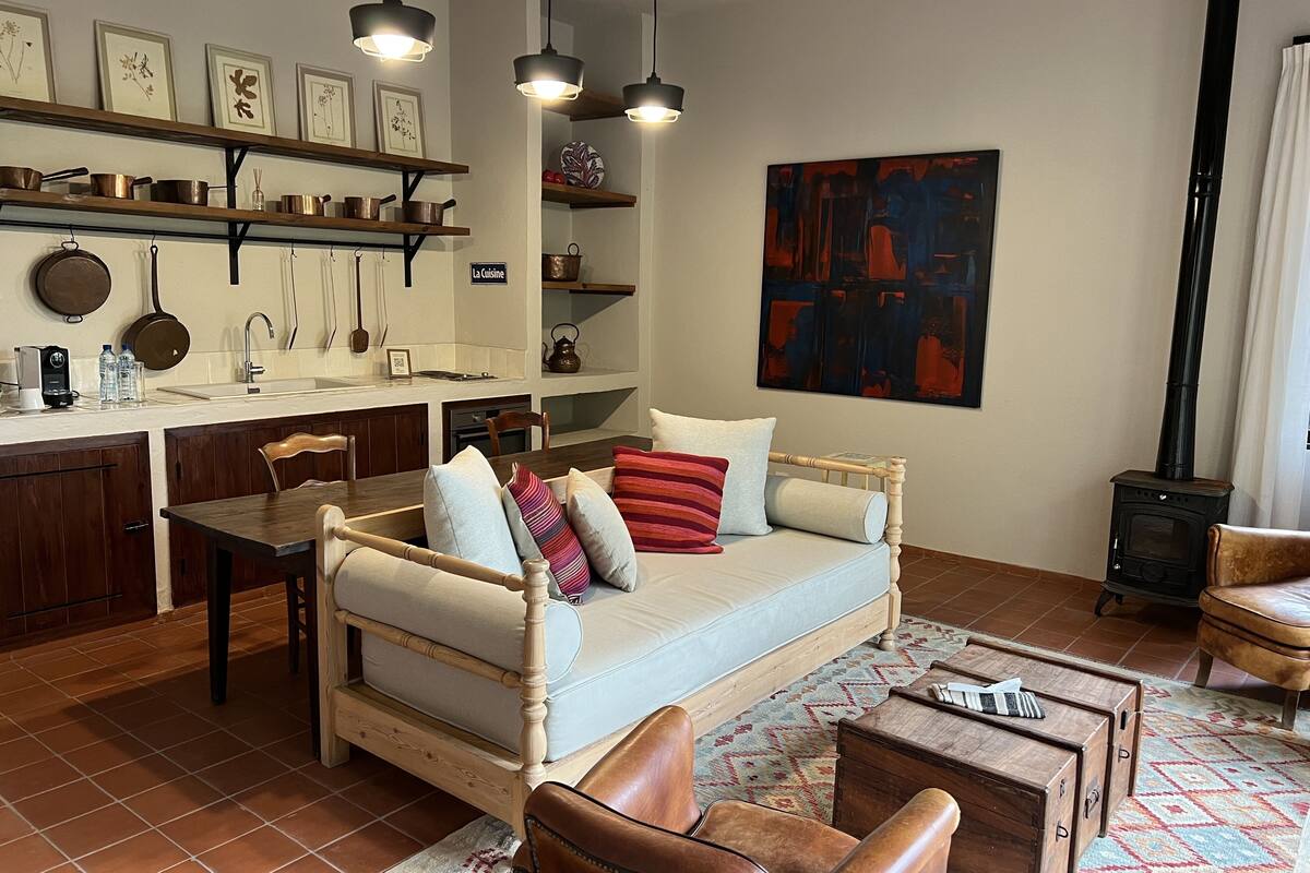 Ein gemütliches Wohnzimmer mit einer Holzsofa, einem Esstisch und einer Küchenzeile mit Regalen und hängendem Kochgeschirr.