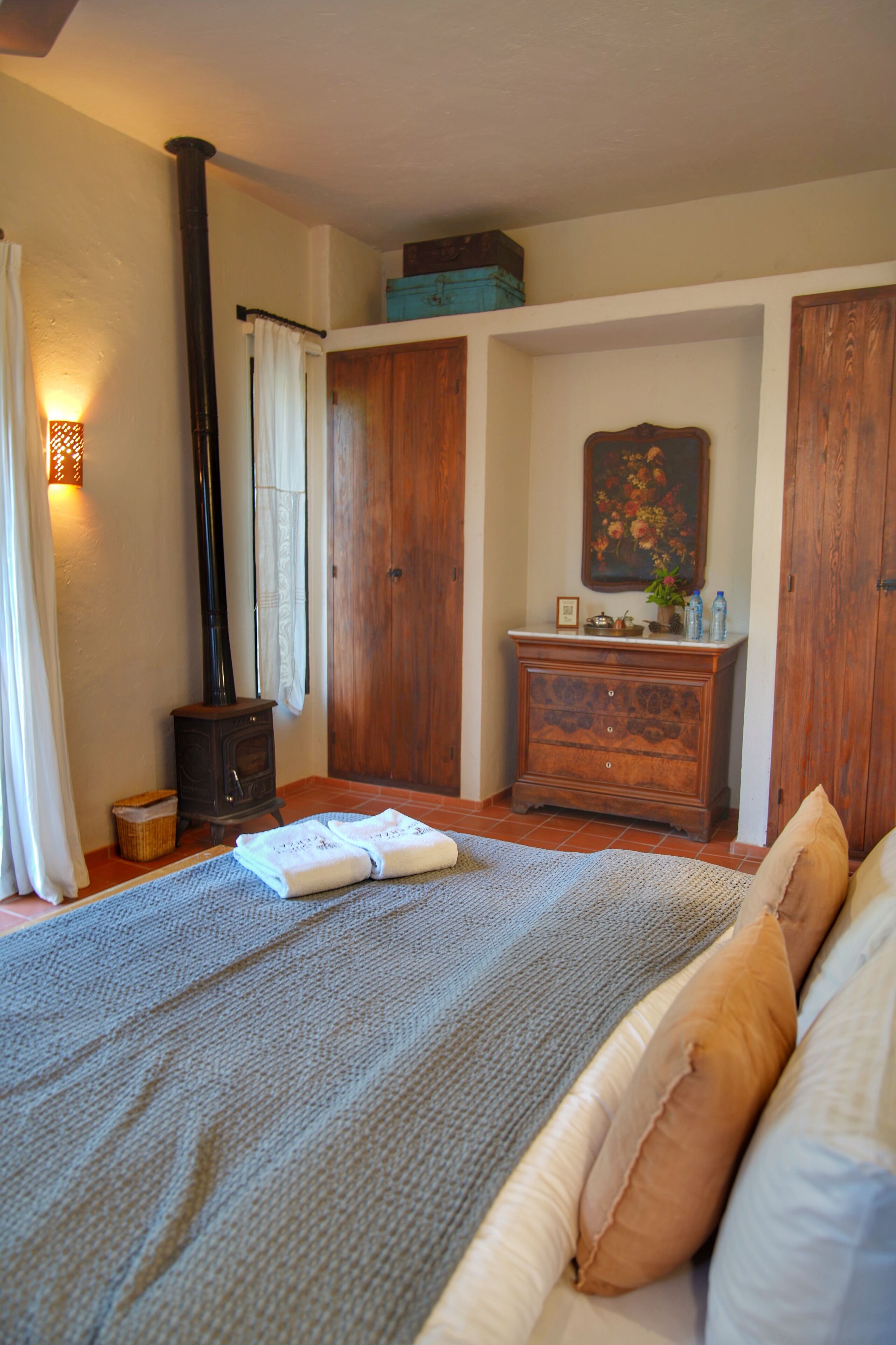 Um quarto com cama, cómoda, quadro, guarda-roupa de madeira e lareira a lenha.