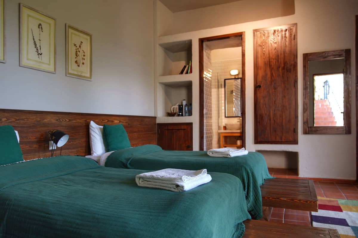 Ein Hotelzimmer mit zwei Betten, einem Holzkopfteil, einem Badezimmer mit Spiegel und einer Tür zu einem weiteren Raum.