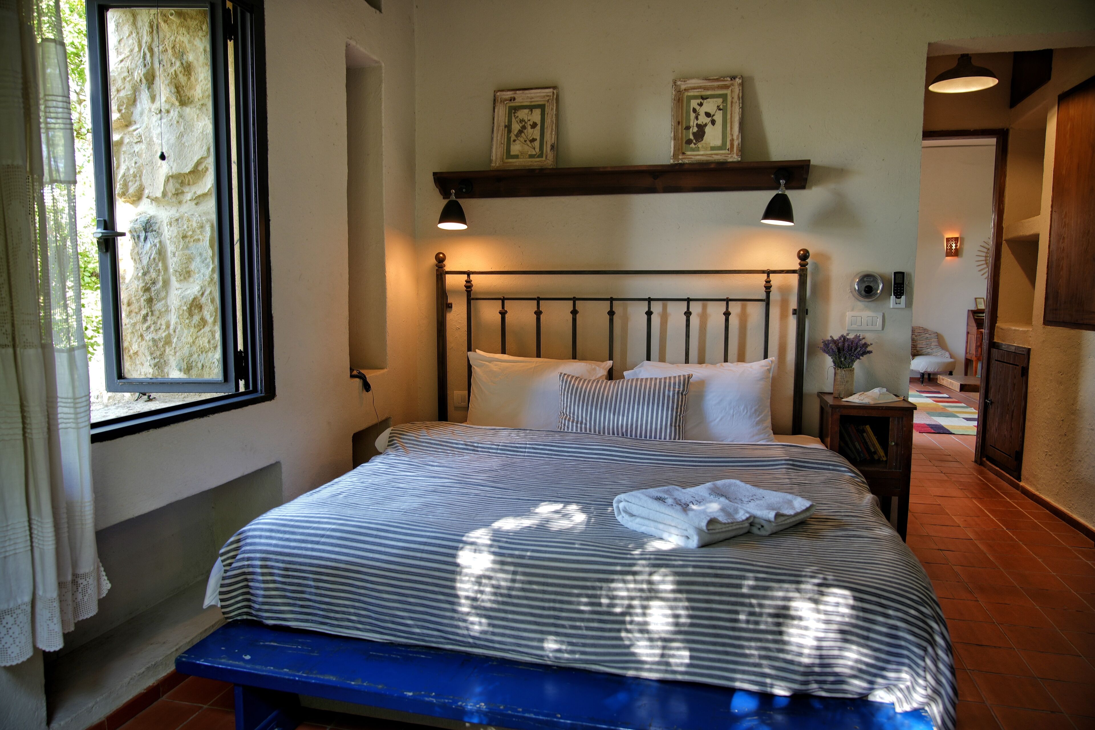 A neatly made bed with striped bedding, a bench at the foot of the bed, and a window with curtains.