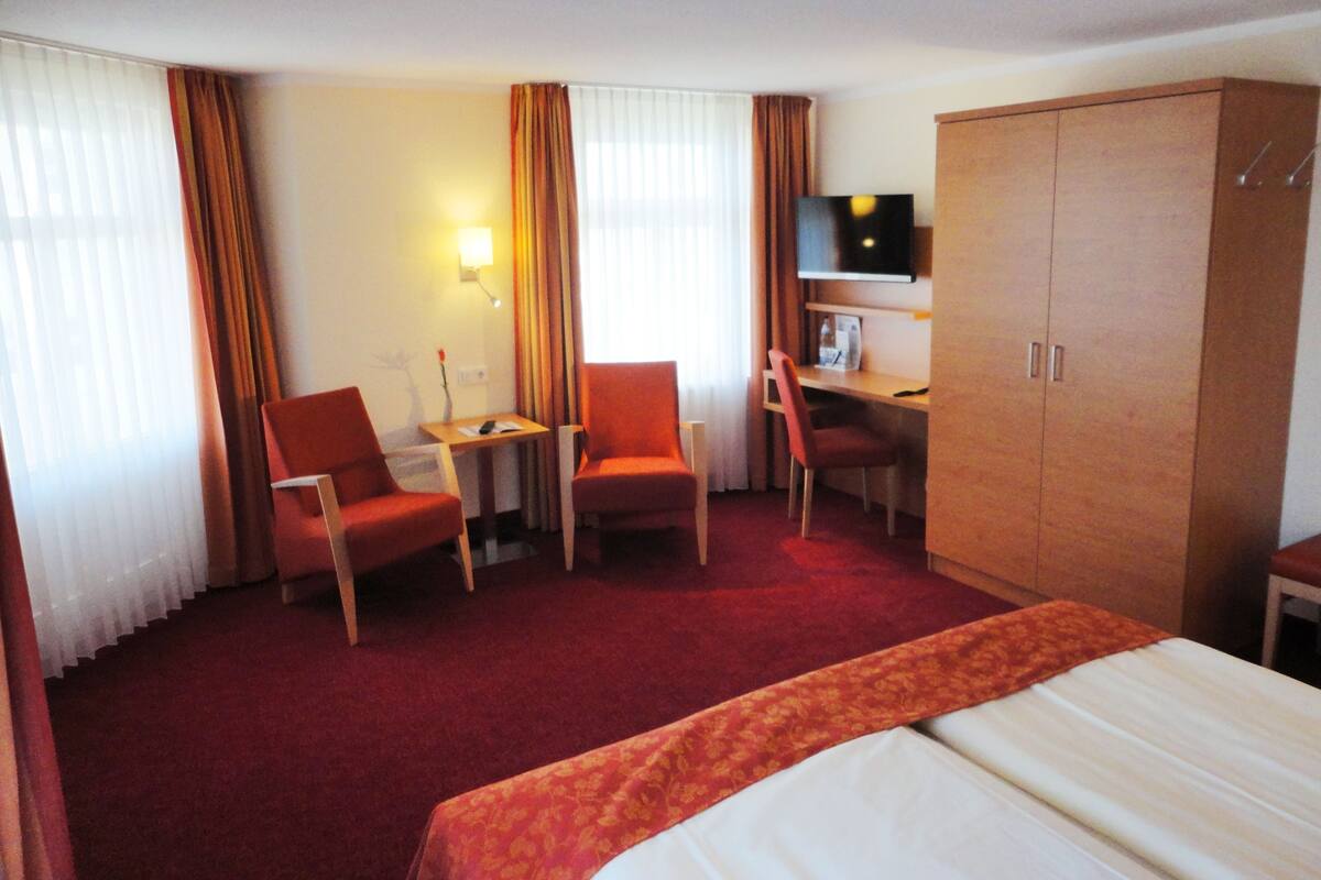 Una habitación de hotel con una cama, dos sillones, un escritorio, un televisor y un armario.