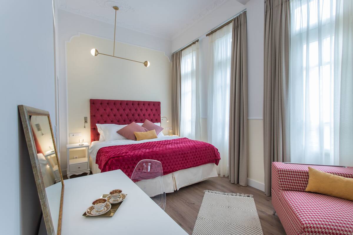 Un dormitorio moderno con una cabecera roja, una mesita de noche blanca con espejo, y un sofá rojo y blanco a cuadros.